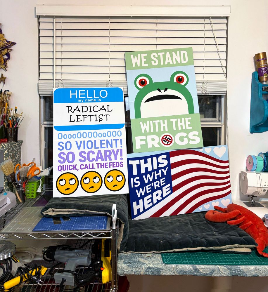 Protest signs for October NO KINGS! "Hello my name is RADICAL LEFTIST. OoooOOOooo, so violent, so scary, quick call the feds" |  "WE STAND WITH THE FROGS"  |  waving American flag with white text "THIS IS WHY WE'RE HERE" replacing the stars.