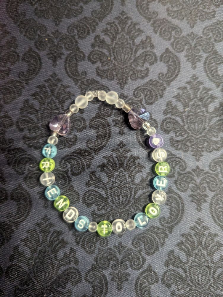A beaded bracelet reading "friends to lovers" in pastel beaded lettering.