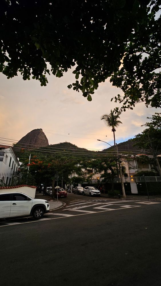 Uma rua, uns carros e atrás pode ver o morro e o bondinho do pão de açúcar