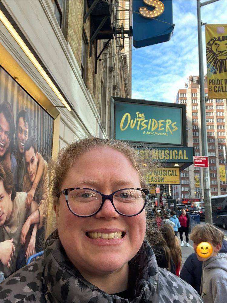 A selfie of Mary in front of The Outsiders marquee.