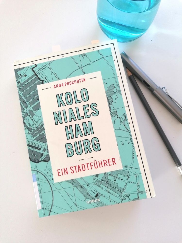 Anna Prochottas "Koloniales Hamburg: Ein Stadtführer" neben einem Glas und zwei Stiften