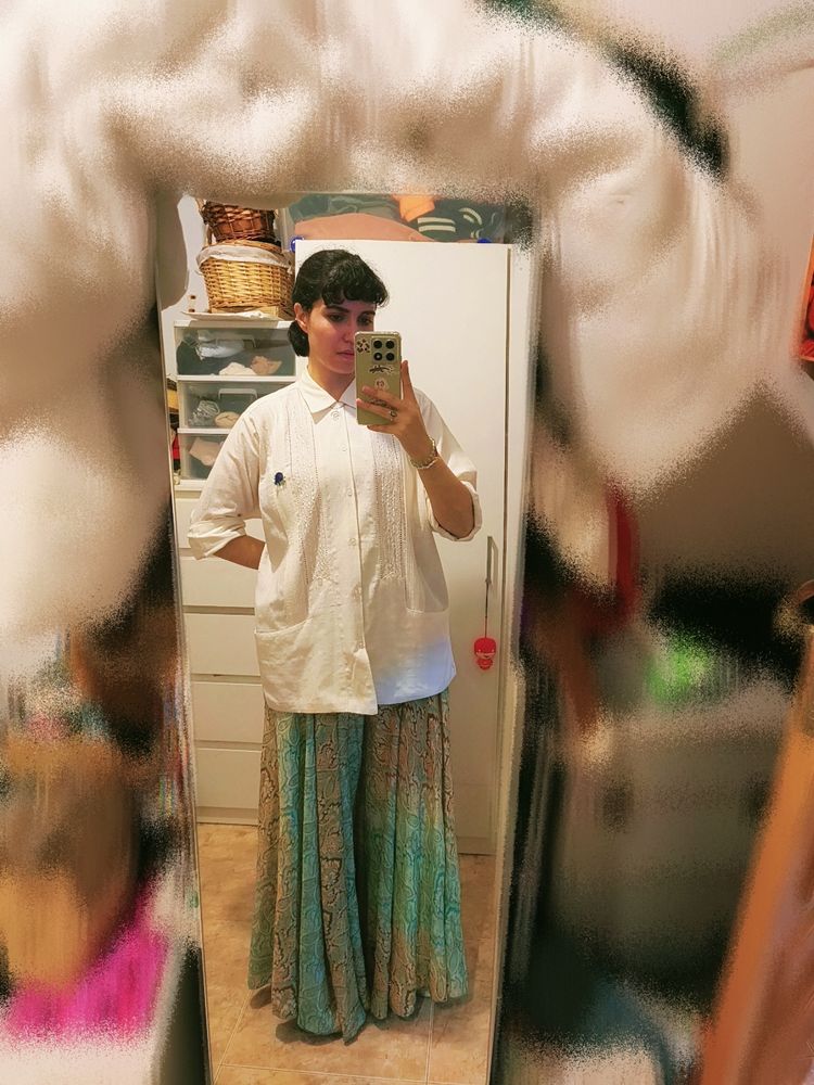 Selfie en el espejo para enseñar un conjunto de ropa que incluye: guayabera blanca con bolsillos bajos, un pantalón estilo falda de vuelo con estampados verdes y dorados, y unas deportivas blancas.