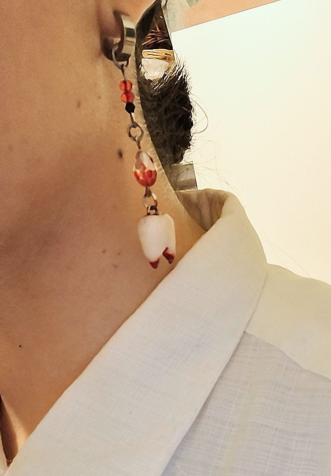 Pendiente de aro plateado con cuentas negras y rojas colgando, con un diente modelado manchado de sangre