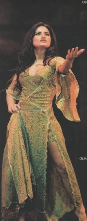Fotografía de una adulta Lola Ponce como Esmeralda, en un vestido verde con gran escote, entallado hasta la cadera, con una raja en la falda enseñando una de las piernas