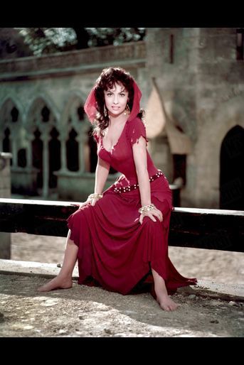 Fotografía de una adulta Gina Lollobrigida como Esmeralda, en un vestido rojo con gran escote y entallado hasta la cadera