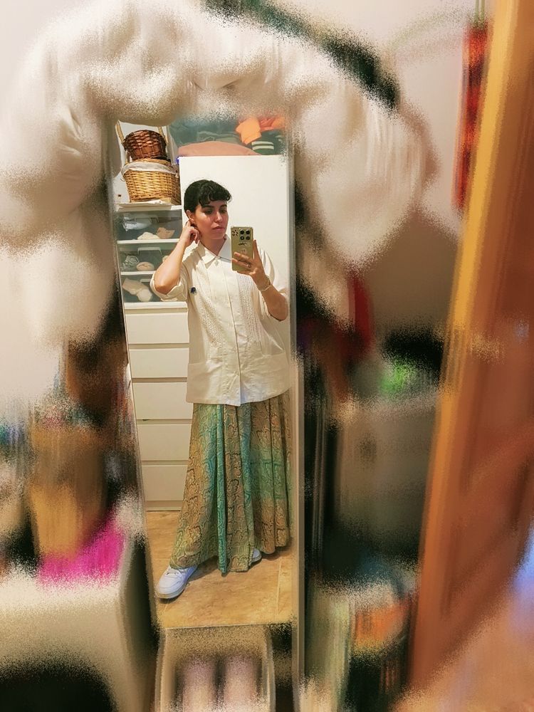 Selfie en el espejo para enseñar un conjunto de ropa que incluye: guayabera blanca con bolsillos bajos, un pantalón estilo falda de vuelo con estampados verdes y dorados, y unas deportivas blancas.