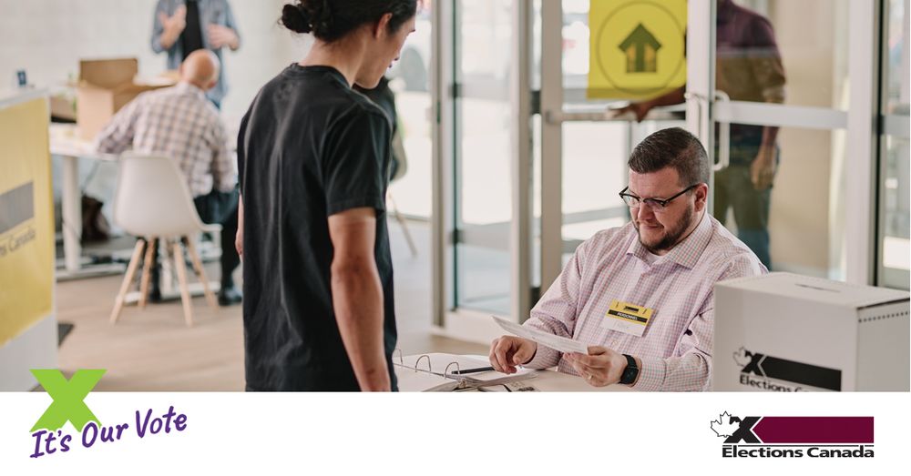 Person is standing at a table while an Elections Canada employee verifies their information. The ballot box is on the table. 