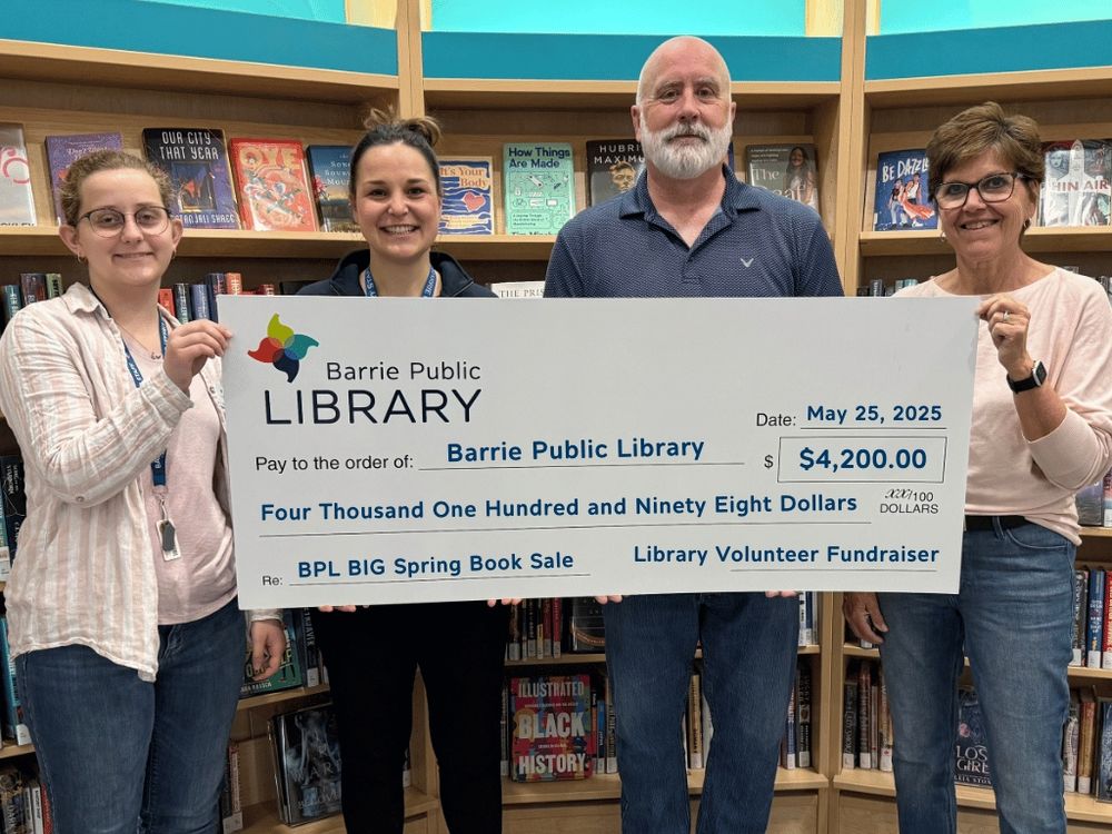 Library staff holding a cheque of the BIG Spring Book Sale proceeds.
