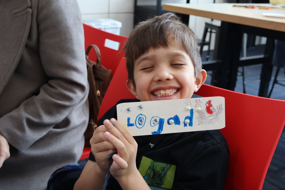 A child holding up a homemade bookmark in Creative Spaces. 