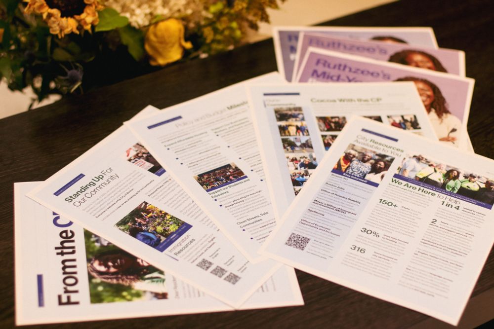 Multiple printed documents laid out on a wooden surface, showing the inside pages of what appears to be a mid-year review or newsletter. The pages contain various sections with photographs, text content, statistics, and infographics. Notable elements include sections titled “Standing Up for Our Community” and other policy-related content with accompanying images of community events and meetings.