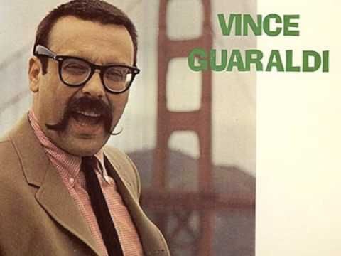 Vince Guaraldi in front of the Golden Gate Bridge with a handlebar mustache and skinny tie jovially winking at you