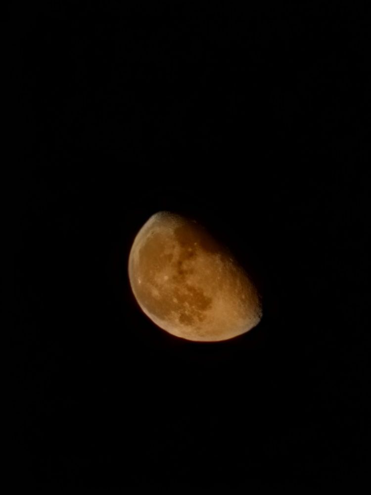 Close up of the moon and its craters with an orange glow, against the pitch black backdrop of the night sky 