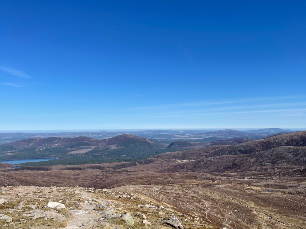 View from Cairngorm plateau under blue sky. Loch Morlich in distance.