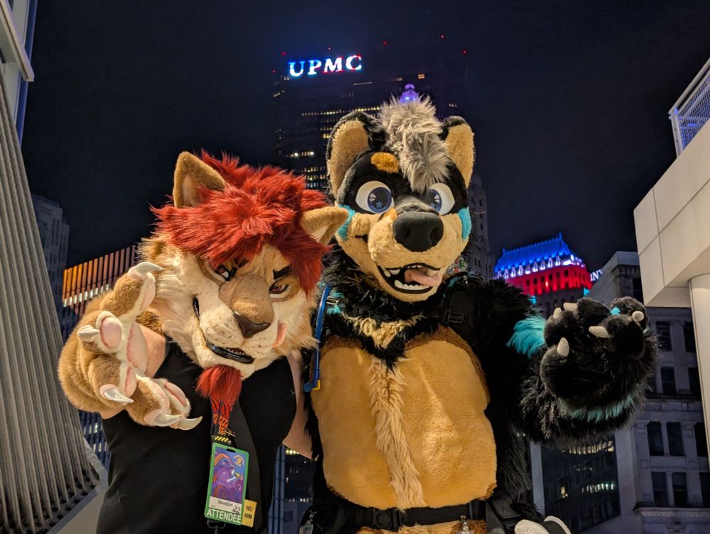 Koi and @revelionart.bsky.social‬ on a balcony with the Pittsburgh skyline in the background