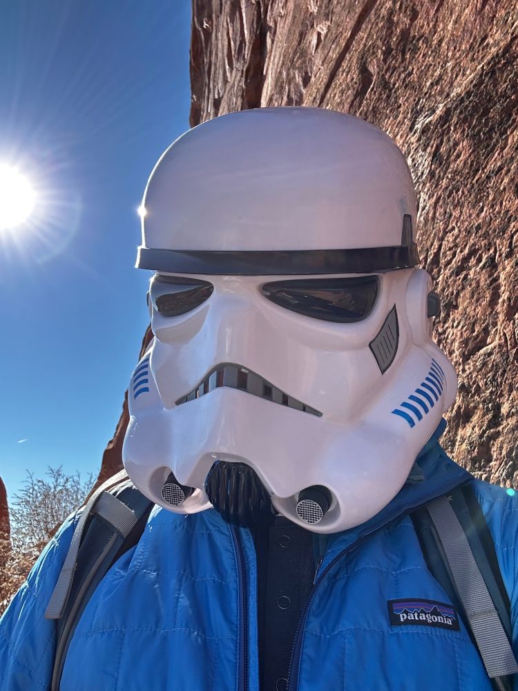 The same stormtrooper stands in front of a vertical red rock wall.