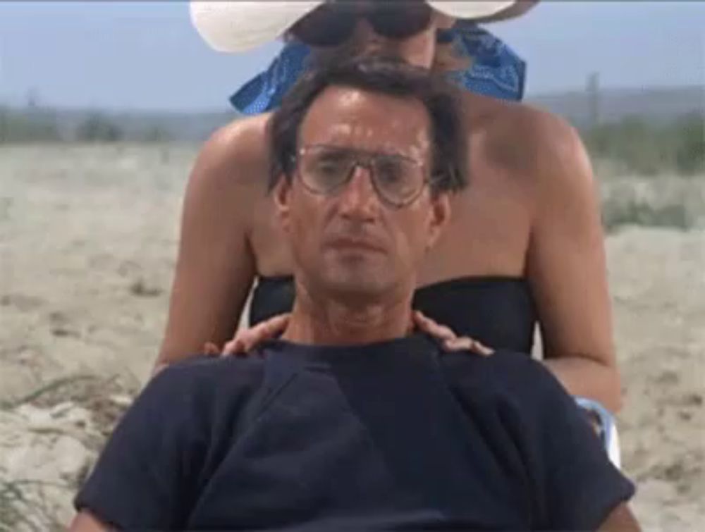 a man wearing glasses is getting a massage from a woman on the beach .