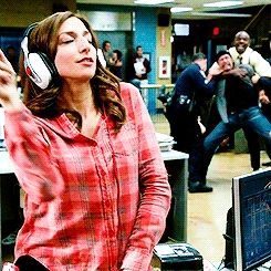 Cena animada da série Brooklyn 99 em que uma garota dança com fones de ouvido enquanto policiais ao fundo se aglomeram para conter um homem.