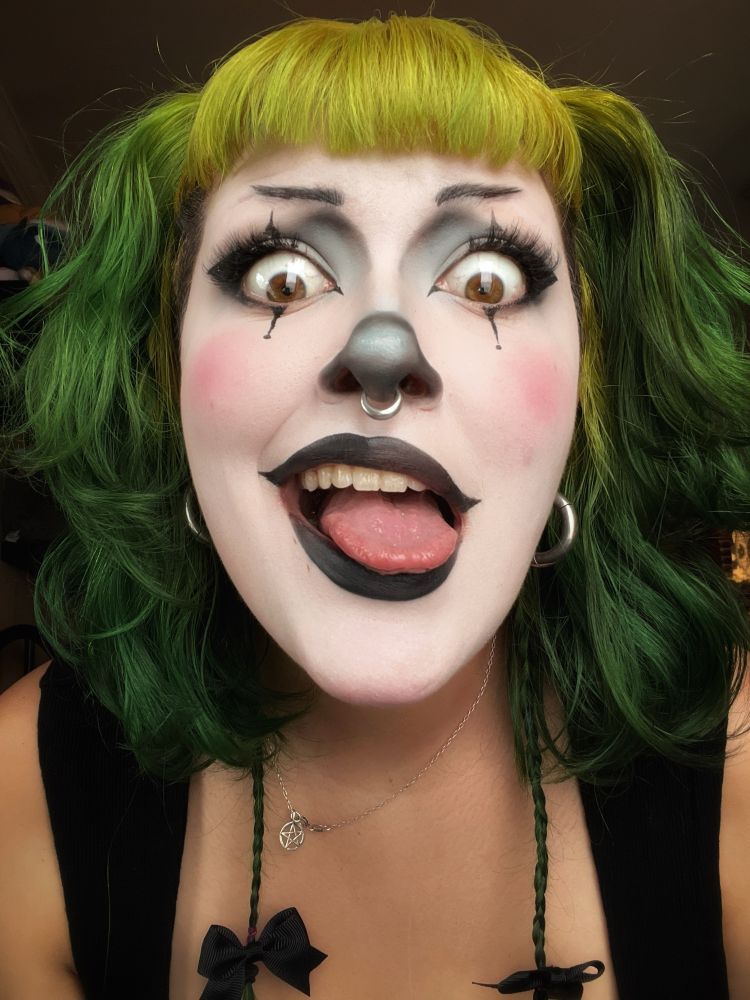 a close selfie picture of Treez, a green haired bitch with clown makeup on. They are making a silly face and have cute little bows on the ends of their braids. The clown makeup is mostly black and white with bits of baby blue around the eyes and the tip of the nose. Their cheeks are softly blushed and their eyes are freakishly large, staring at you through the screen almost