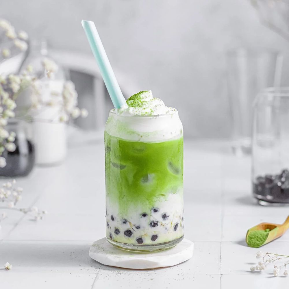 photograph of matcha bubble tea in a glass, topped with whipped cream and matcha powder