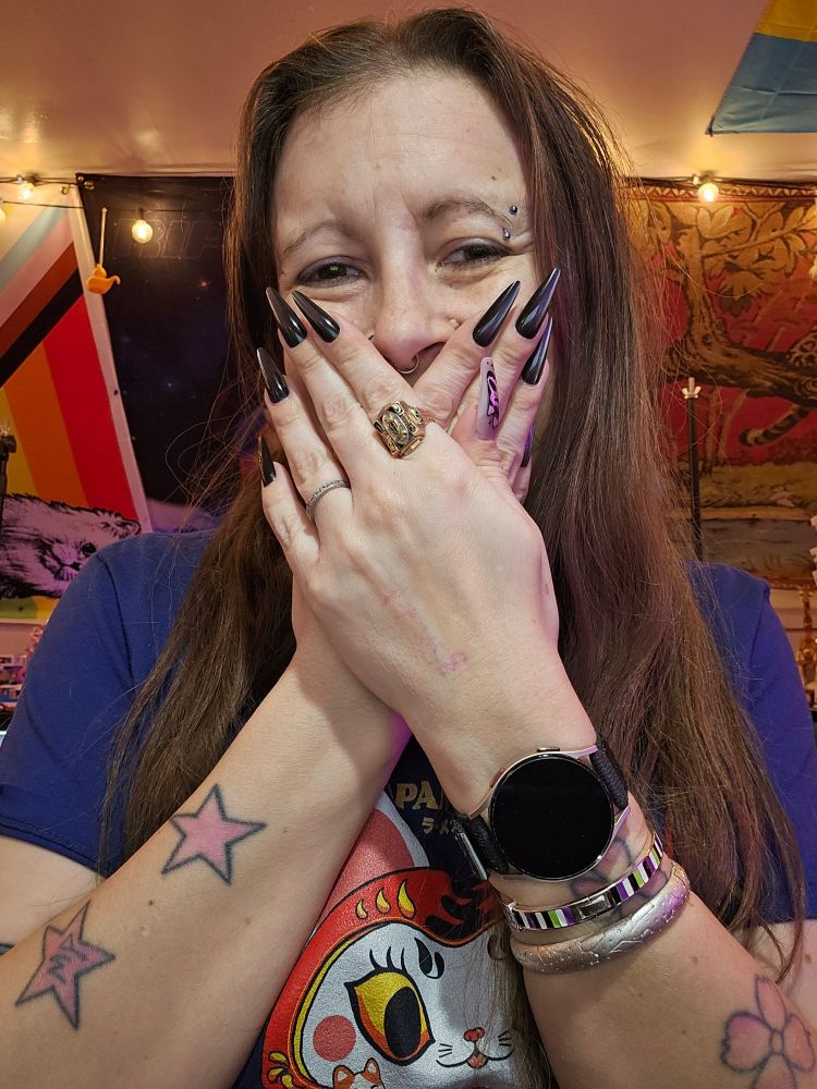 A woman covering her mouth with her hands and she is wearing long nails. 