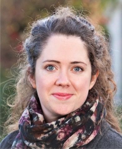 Photo of Professor Hannah Daly. Image shows a woman with long wavt brown hair and fair complection. She is wearing a scarf and a brown coat. Picture is taken outside.
