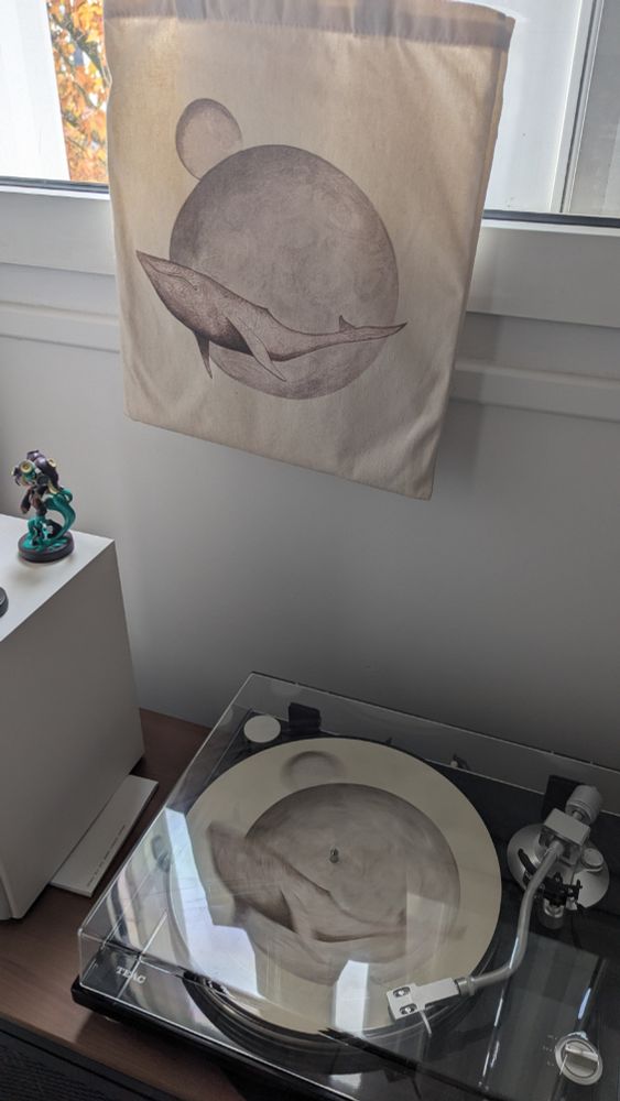 Un tot bag From Mars to Sirius de Gojira, surplombant une platine qui joue un vinyle avec la même image imprimée : une baleine blanche avec des planètes en arrière plan.