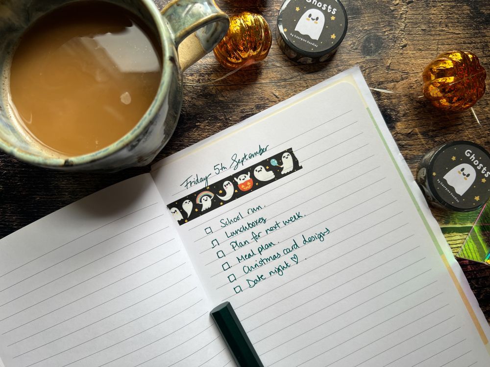 A photograph of a flatlay, featuring a cup of coffee, a notebook with today's to-do list planned out, using cute ghost themed washi tape