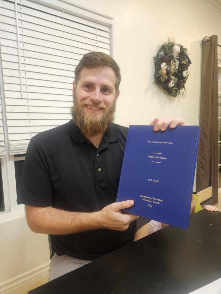 Man in black shirt holding hard cover blue book with silver writing.