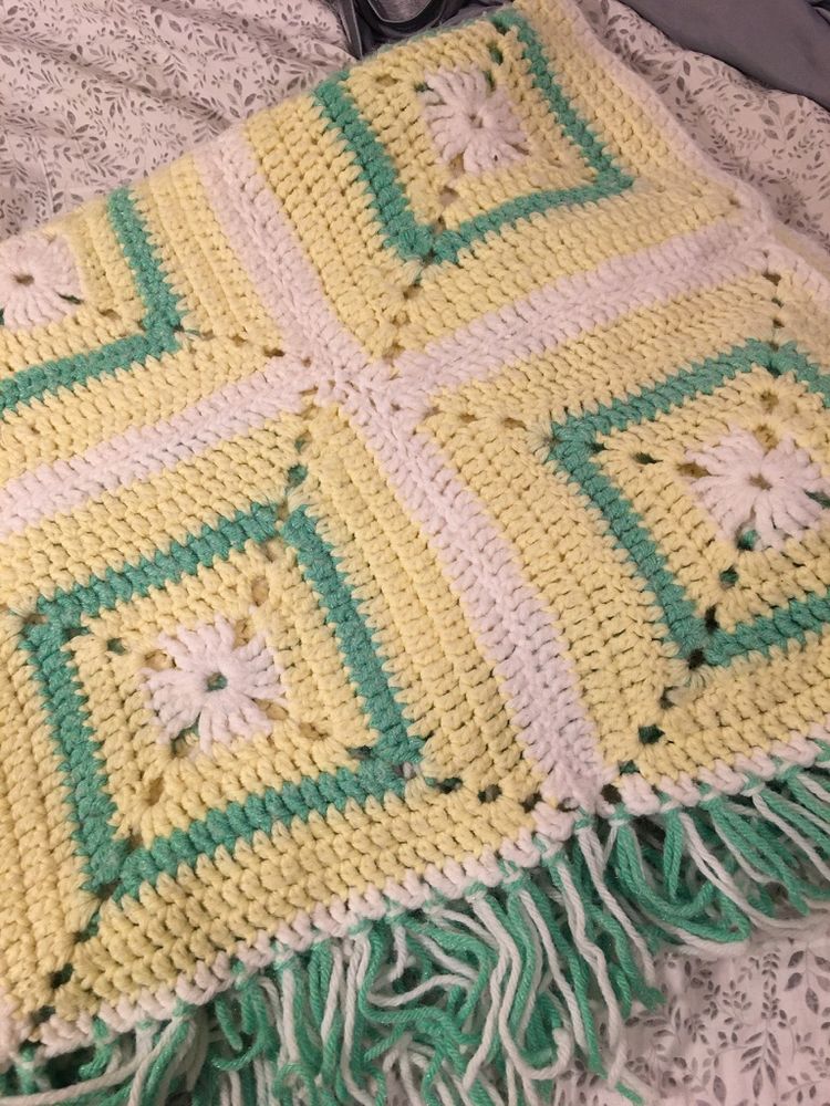 Close up of a yellow and mint green granny square hand crocheted afghan.