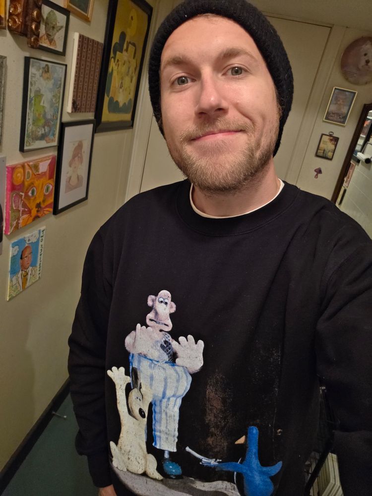 A picture of me wearing a Wallace & Gromit sweatshirt that also features Feathers McGraw holding them at gunpoint 