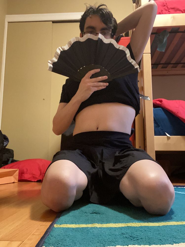I am wearing a short skirt and kneeling as I cover my face with a fan