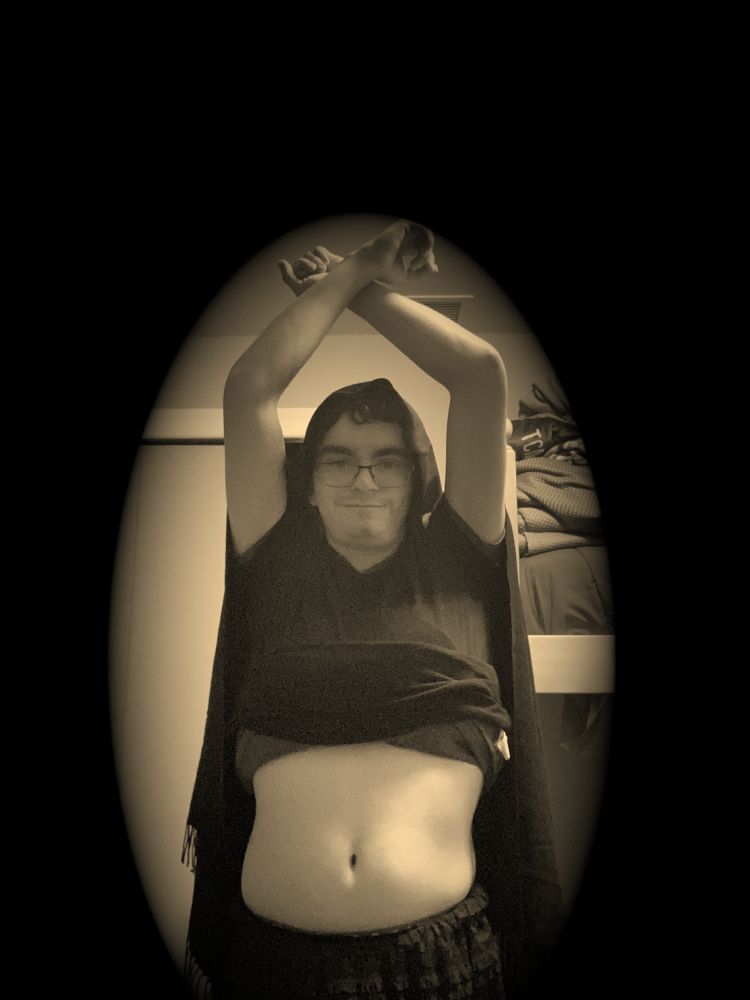 I am wearing a black outfit and veil as I hold my hands over my head; the image is in a sepia filter and framed so that I am inside an oval shading