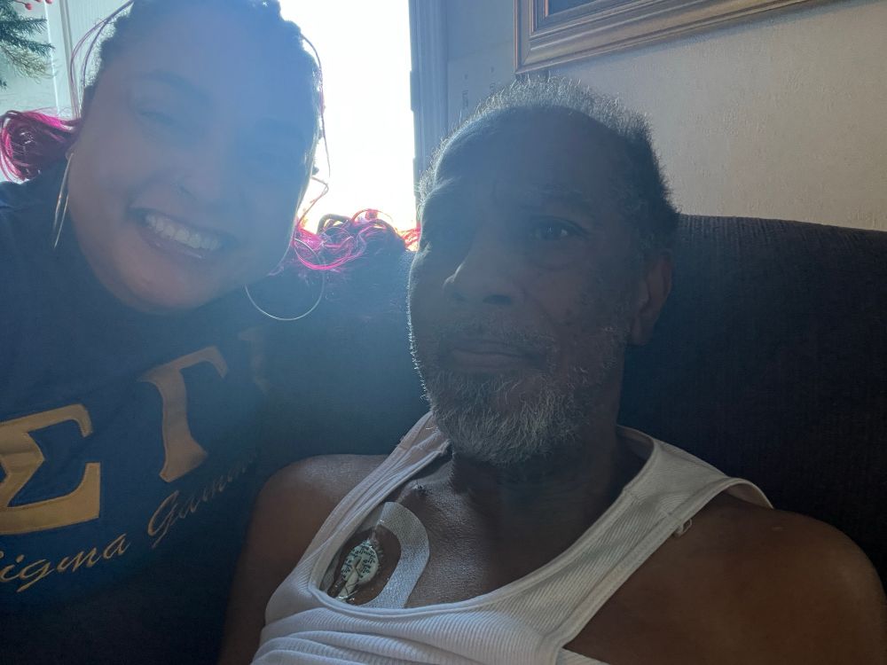 Blurry? Photo of Black woman with an elder Black man. She's smiling and he had a closed mouth slight smile. 