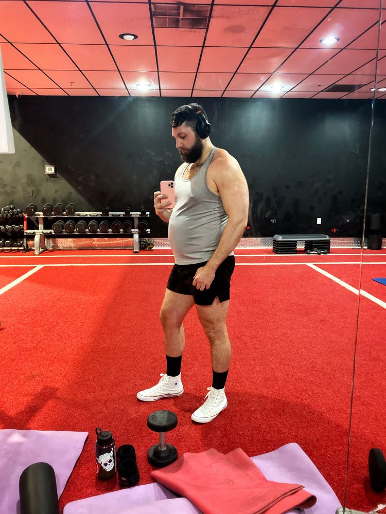 Man posing in the gym mirror after his chest day workout flexing his muscles and showing off his big muscle belly.