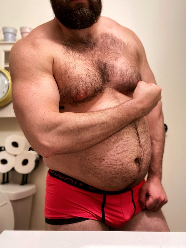 Shirtless man flexing his bicep and showing off his big belly wearing pink underwear.