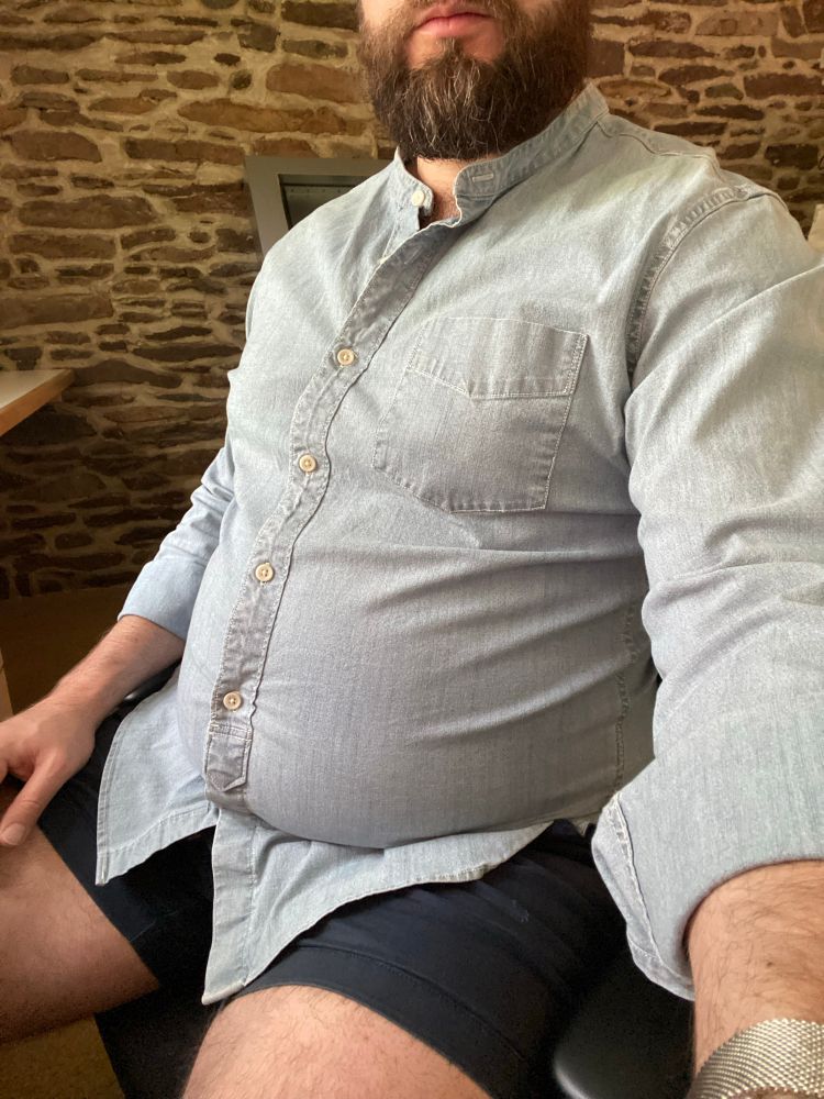 Man wearing a denim button down shirt that is too small and stretched across his big belly.