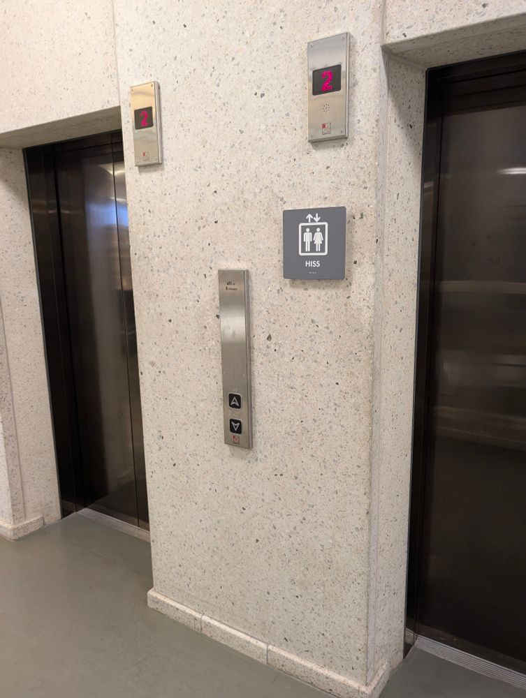A pair of lifts with a sign saying "HISS" outside of them.