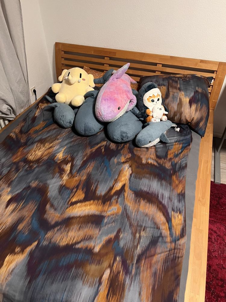 A cozy bed with lots of plushies, primarily sharks, on it