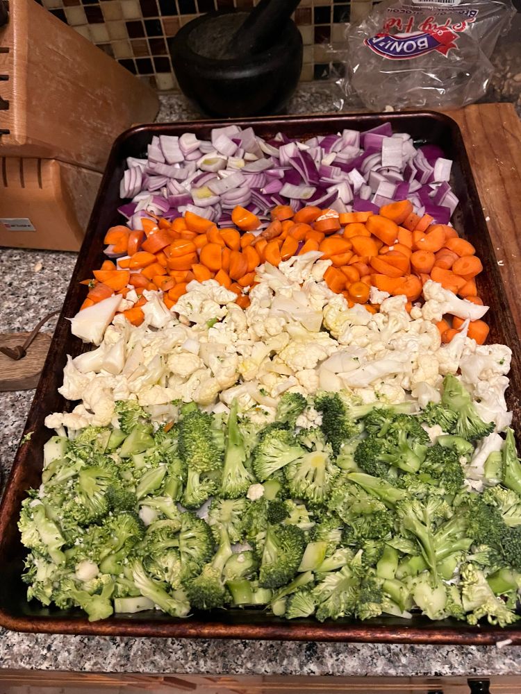 A cookie sheet of raw vegetables organized by color: purple onions, orange carrots, white cauliflower and green broccoli about to be roasted 