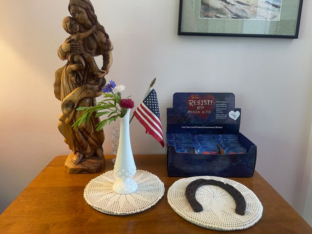 A table with a statue of Mary and baby Jesus, a white hobnail glass bud vase with red, white & blue bachelor buttons and mountain mint, an old horse recently found in the yard, a little US flag 🇺🇸 in a glass toothpick holder, and a box of Resist Trial Bags (Hand-mixed from: Black pepper, salt, paprika, cayenne red pepper, white pepper, chipotle pepper) that Penzeys sent me to give away to people.

Penzeys gave me this RESIST because my “backyard is where America’s fate is to be determined.” I have a mission to share the RESIST “with people in need of a tasty seasoning to brighten their day.”