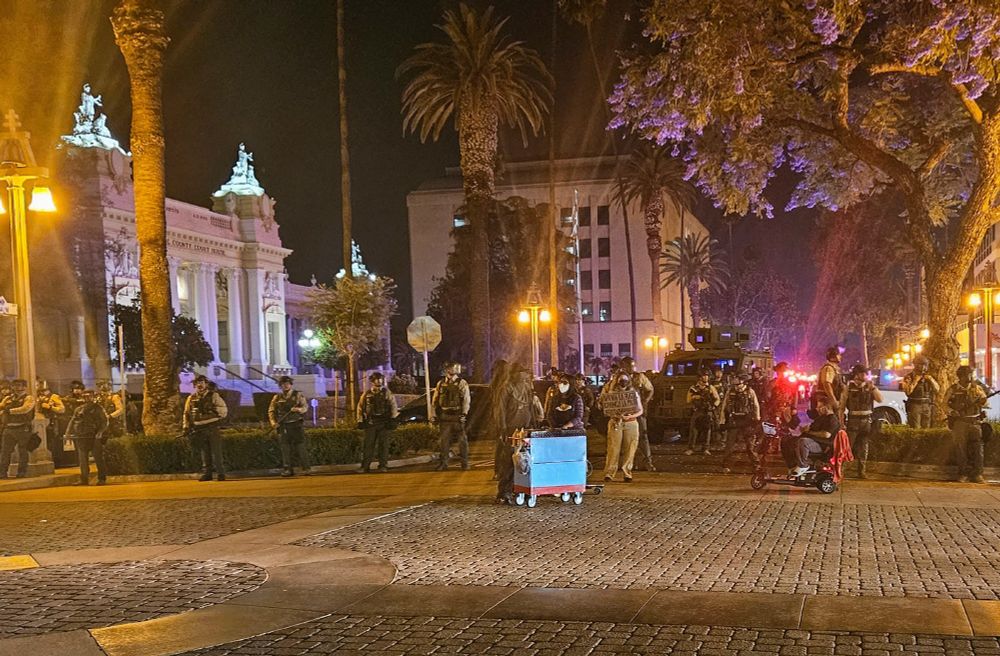 A vendor sells elote in front of an unnecessary display of force by the Riverside County Sheriff. 