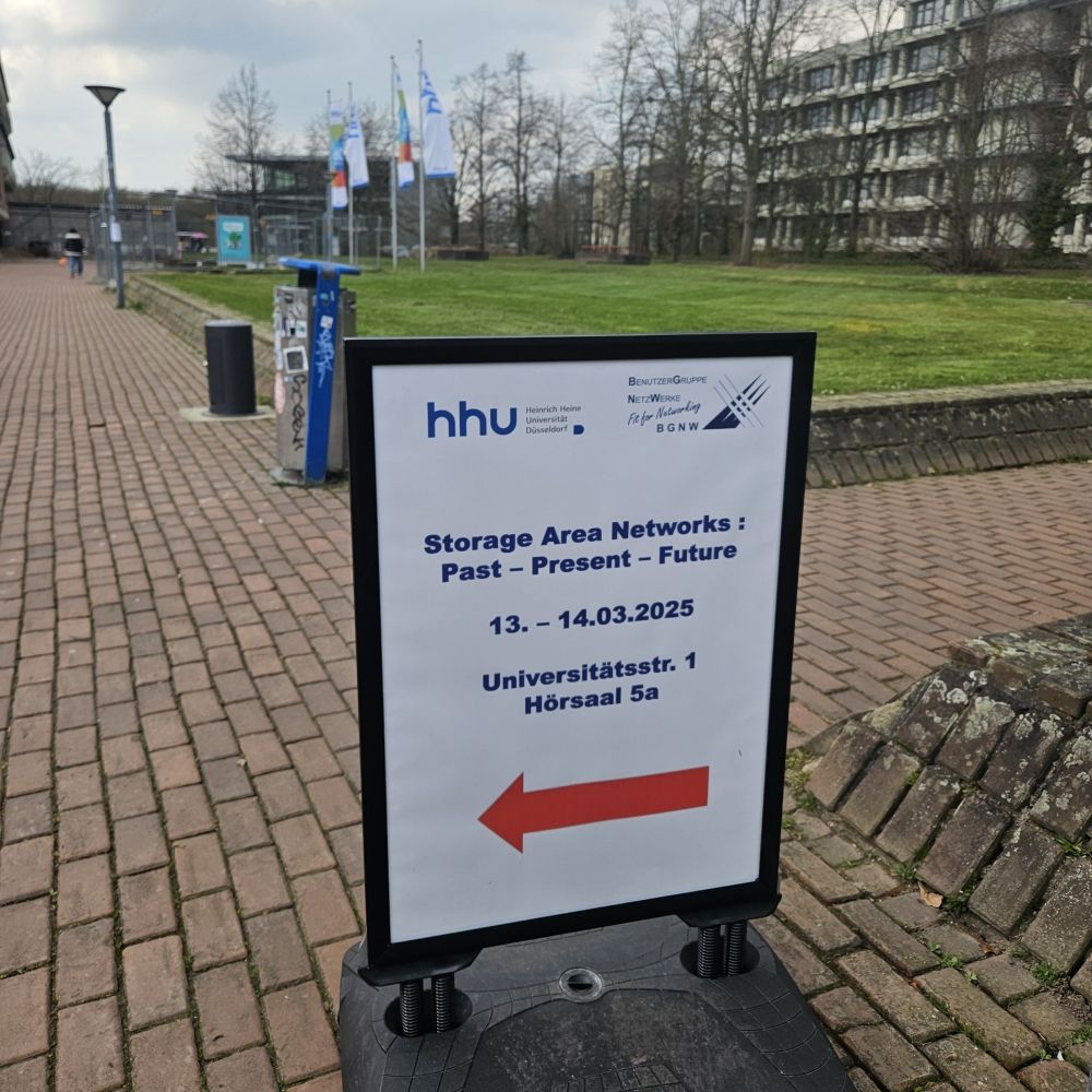 Ein Schild auf dem Campus, mit einer Wiese im Hintergrund, welches zur SAN-Tagung mit einem roten Pfeil nach Hörsaal 5A leitet.