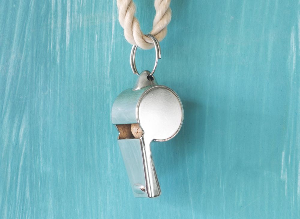 A silver metal whistle hanging from a white rope in front of a light blue background. 