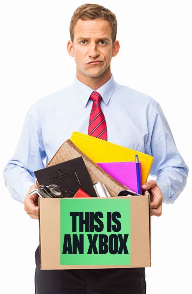 Photo d'un gars en costard qui semble avoir été viré.
Il porte un carton qui contient ses affaires.
Sur le carton est écrit le slogan récent de la marque Xbox "THIS IS AN XBOX"
