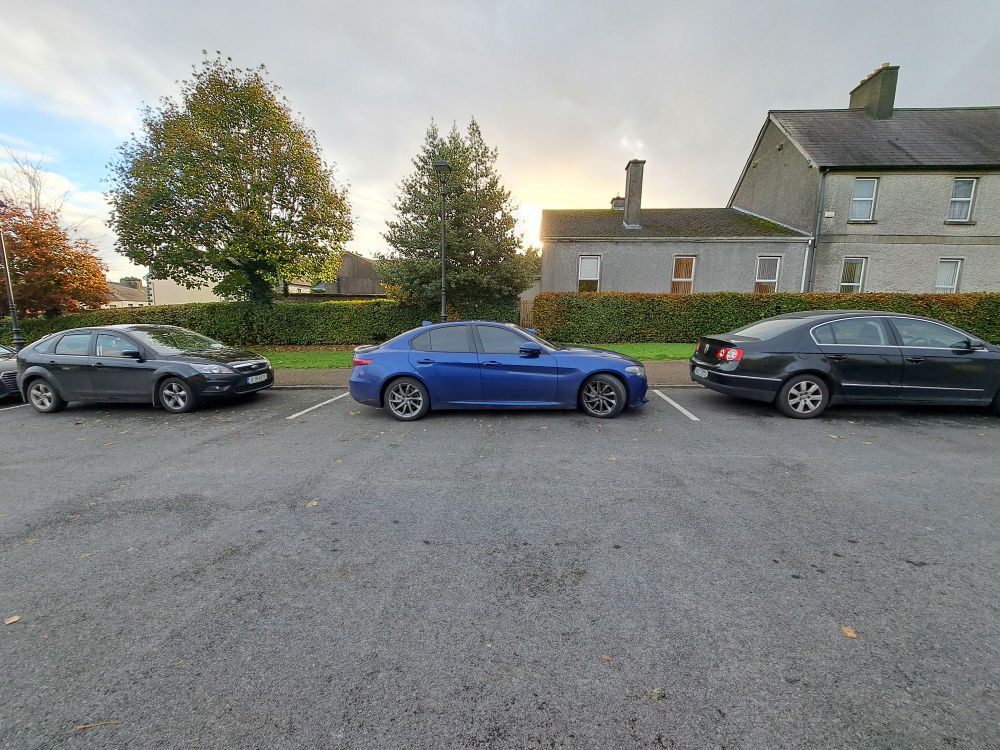 Photograph of three cars in a parking lot. Two on either side of the photo are black, and the one in the middle is blue