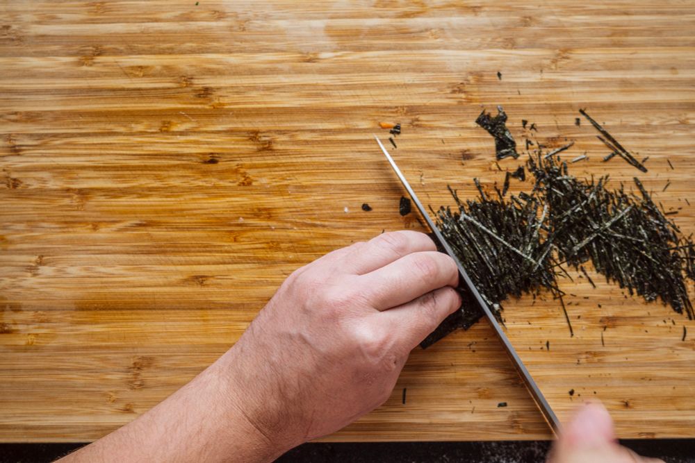 a man finely julienning some nori on a wooden cutting board
