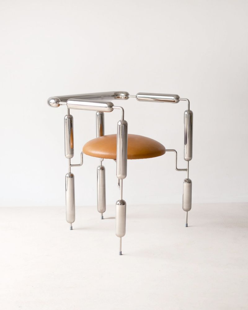 photo of the armchair in the link. It has a silver frame that is minimalist other than thickened sausage-link shaped middle sections, similar to a poodle haircut. It has a tan leather seat.