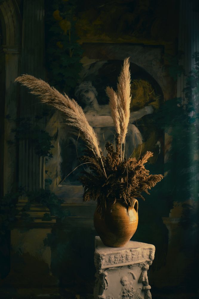 A vase filled with dried flowers sits in front of a mural