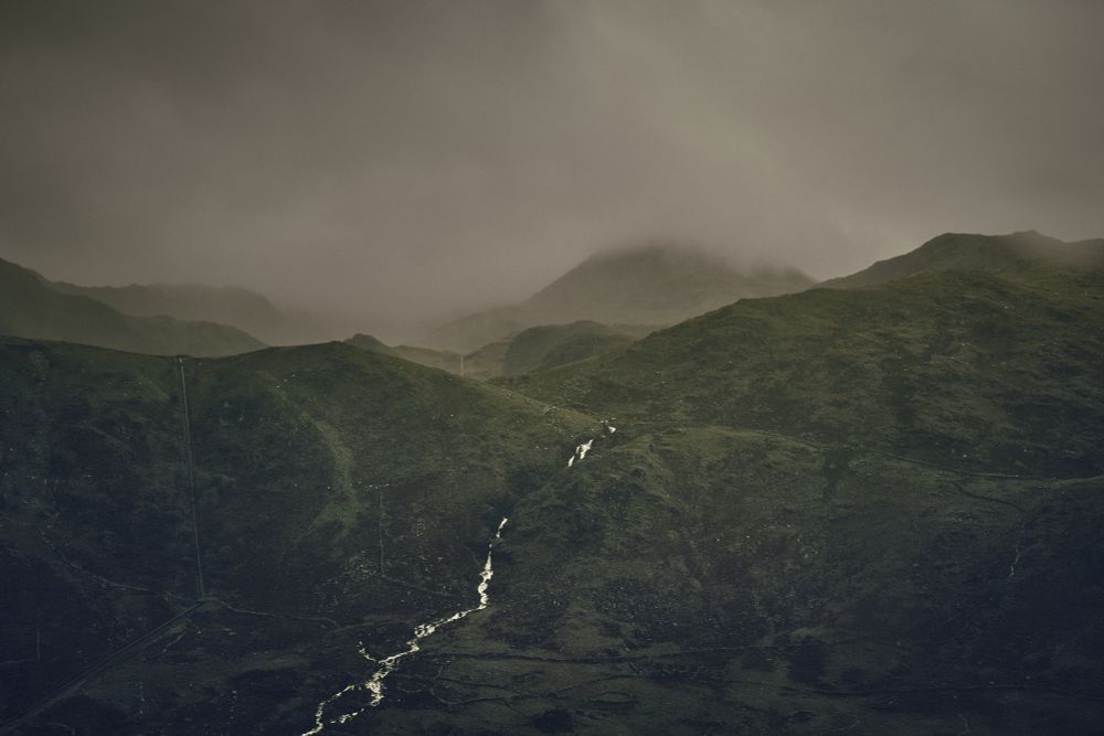 Looking across a deep valley to a range of hills partially obscured by rain and cloud.