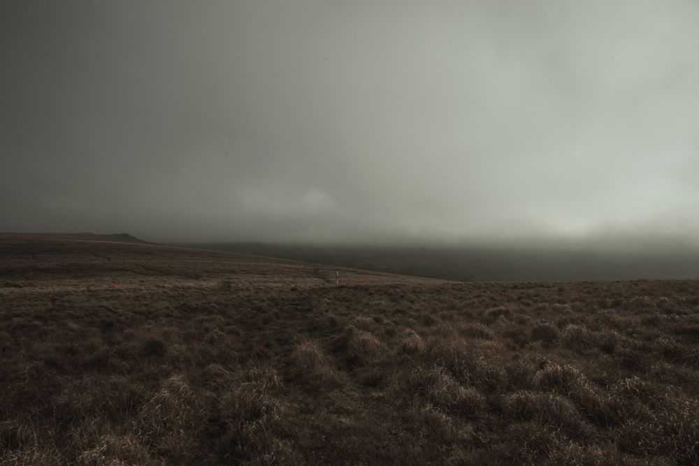 3 photos of northern Dartmoor. In each photo a red and white marker indicates the edge of live firing area. Low cloud predominates in all images. The landscape is largely featureless.